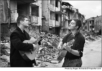 Guitar players in a street marked by the war